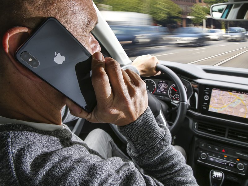 Telefonieren am Steuer ohne Freisprechanlage Mann telefoniert am Steuer eines Autos während der Fahrt mit Smartphone am Ohr.